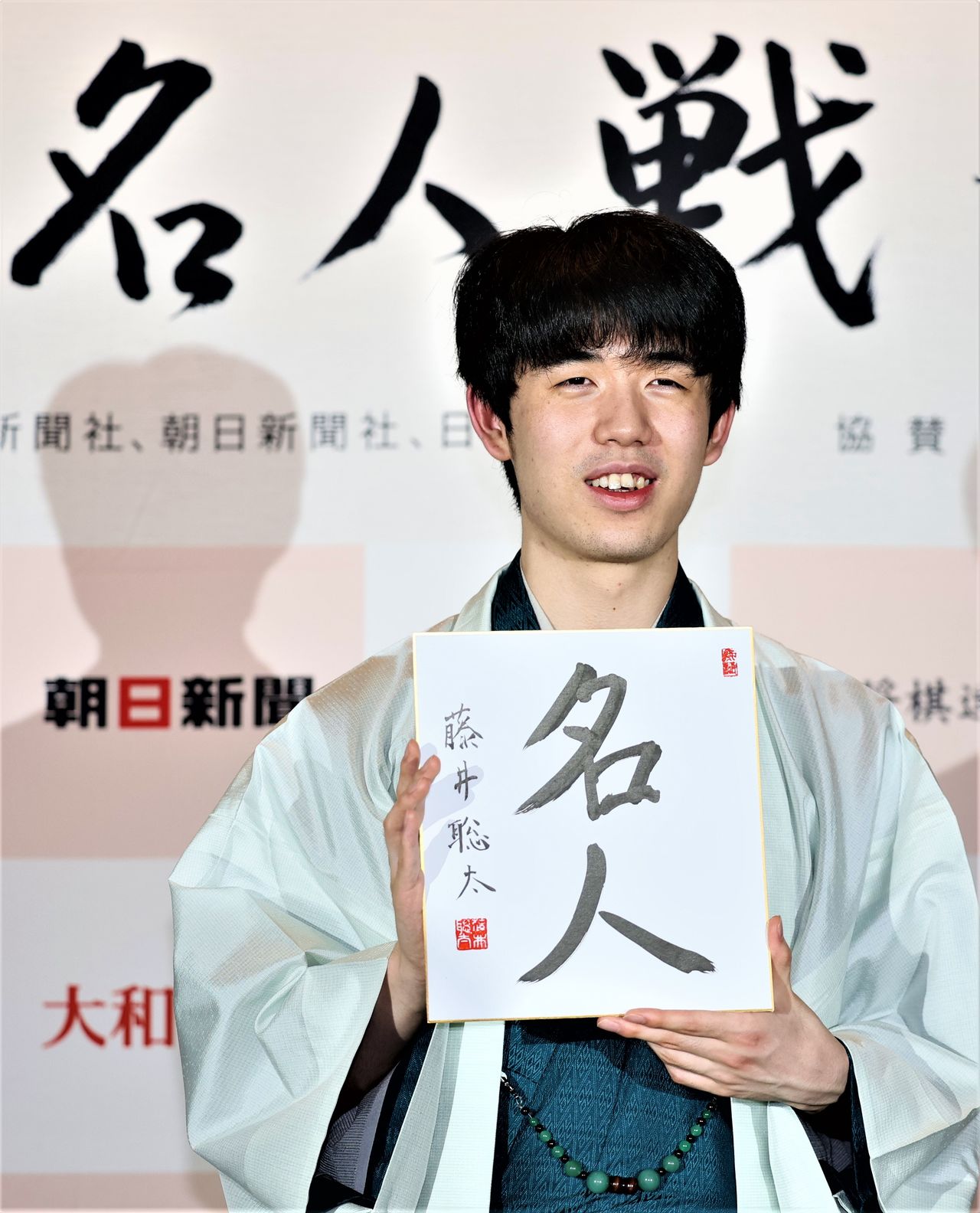 Fujii Sōta holds a card reading “Meijin” at a press conference after winning the title of the same name in Takayama, Nagano Prefecture, on June 1, 2023. (© Jiji)