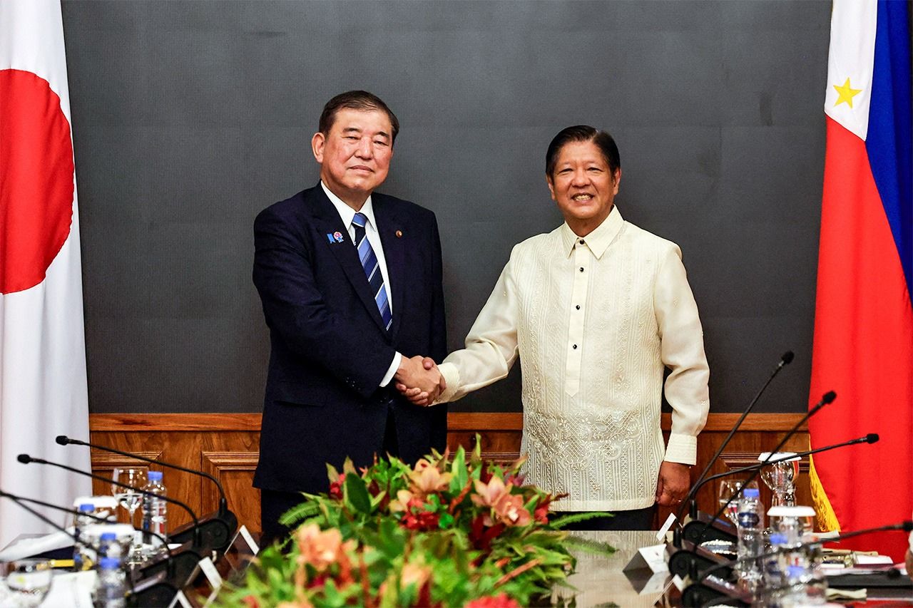Prime Minister Ishiba (left) shakes hands with President Marcos Jr. in Manila. (© Reuters)