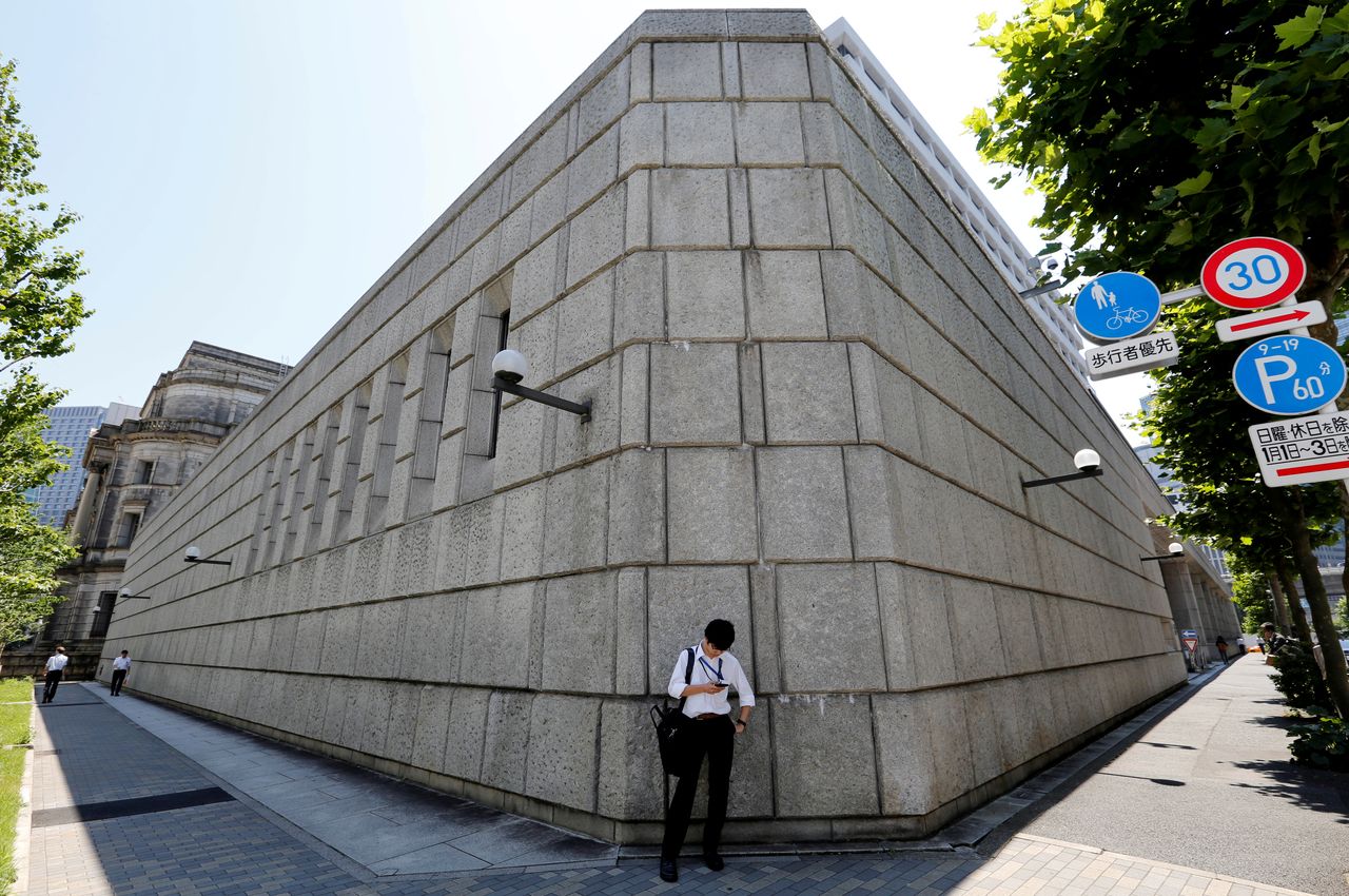 FILE PHOTO: A man looks at a mobile phone in front of the Bank of Japan building in Tokyo, Japan June 16, 2017. REUTERS/Toru Hanai/File Photo
