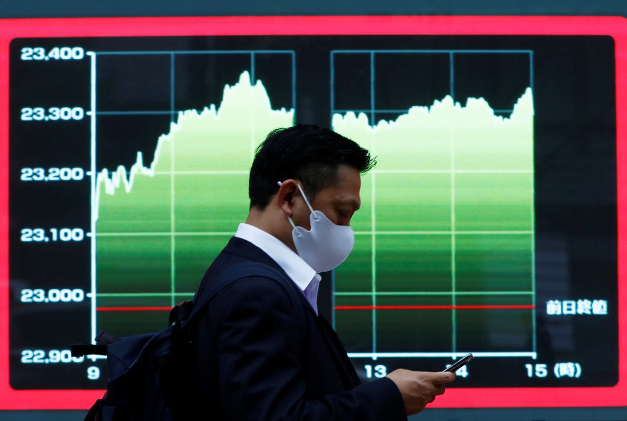 FILE PHOTO: A man wearing a protective face mask walks past a screen displaying a graph showing recent Nikkei share average outside a brokerage, amid the coronavirus disease (COVID-19) outbreak, in Tokyo, Japan November 2, 2020. REUTERS/Issei Kato/File Photo