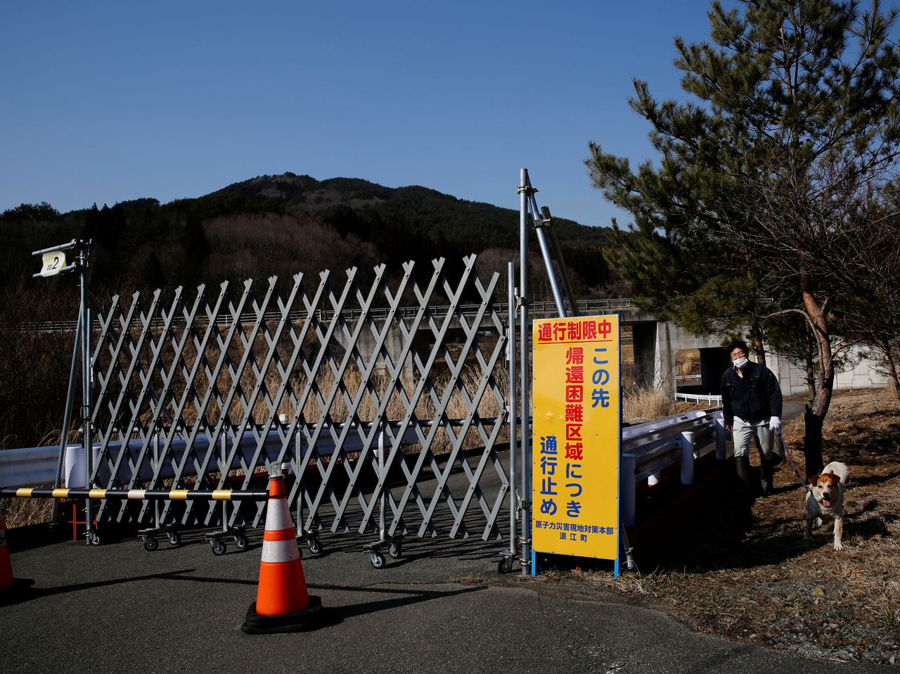 Sakae Kato walks past workers checking radiation levels on a road near his house as he walks Pochi, his dog which he rescued four years ago, in a restricted zone in Namie, Fukushima Prefecture, Japan, February 20, 2021. Kato looks after 41 cats in his home and another empty building on his property. A decade ago, he stayed behind to rescue cats abandoned by neighbours who fled the radiation clouds belching from the nearby Fukushima nuclear plant. He won't leave. I want to make sure I am here to take care of the last one,