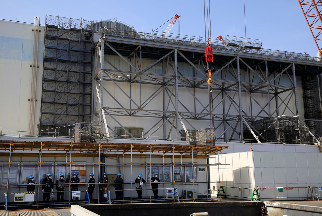 Workers wait at a bus stop in front of No. 3 reactor building at the tsunami-crippled Fukushima Daiichi nuclear power plant in Okuma town, Fukushima prefecture, Japan March 1, 2021. Picture taken March 1, 2021. REUTERS/Sakura Murakami
