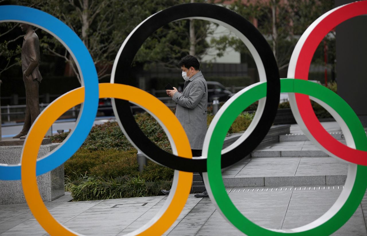 FILE PHOTO: A man looks at his mobile phone next to The Olympic rings in front of the Japan Olympics Museum in Tokyo, Japan, March 4, 2020. REUTERS/Stoyan Nenov