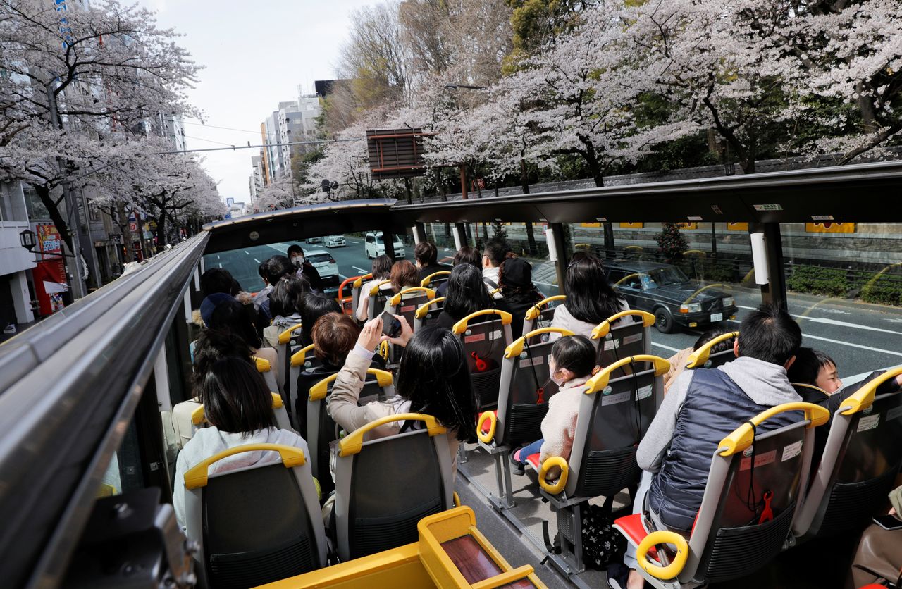 Passengers wearing protective face masks enjoy viewing blooming cherry blossoms from an open-top sightseeing bus, operated by Hato Bus Co., after Japan's government lifted the coronavirus disease (COVID-19) state of emergency in the Tokyo area, in Tokyo, Japan March 22, 2021. REUTERS/Androniki Christodoulou NO RESALES. NO ARCHIVES?