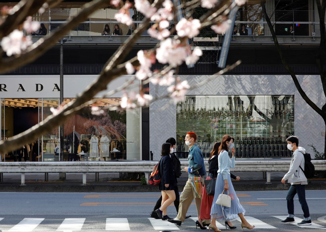 FILE PHOTO: Pedestrians wearing protective face masks amid the coronavirus disease (COVID-19) outbreak, are seen behind cherry blossoms in Tokyo, Japan, March 18, 2021. REUTERS/Kim Kyung-Hoon