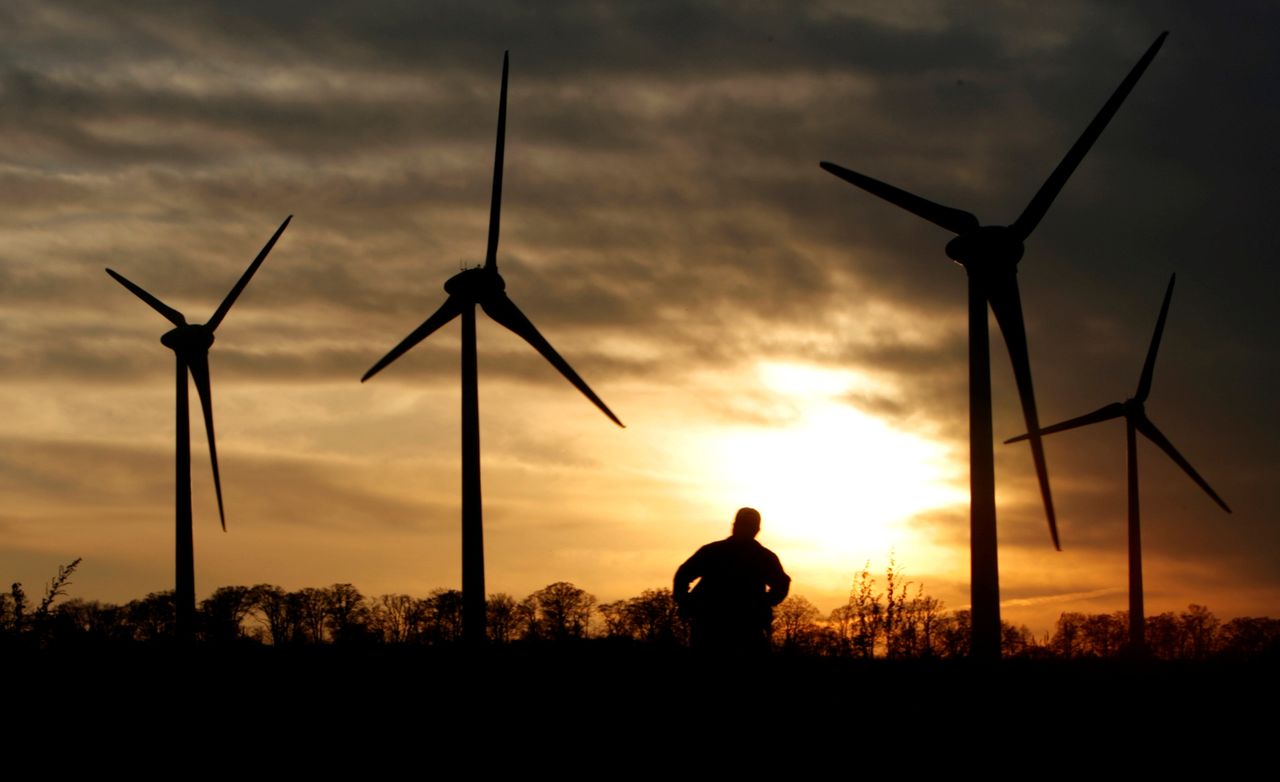 FILE PHOTO: A man looks at 100-metre-tall (328-foot-tall) wind turbines during sunset at the Electric Power Development Co., Ltd