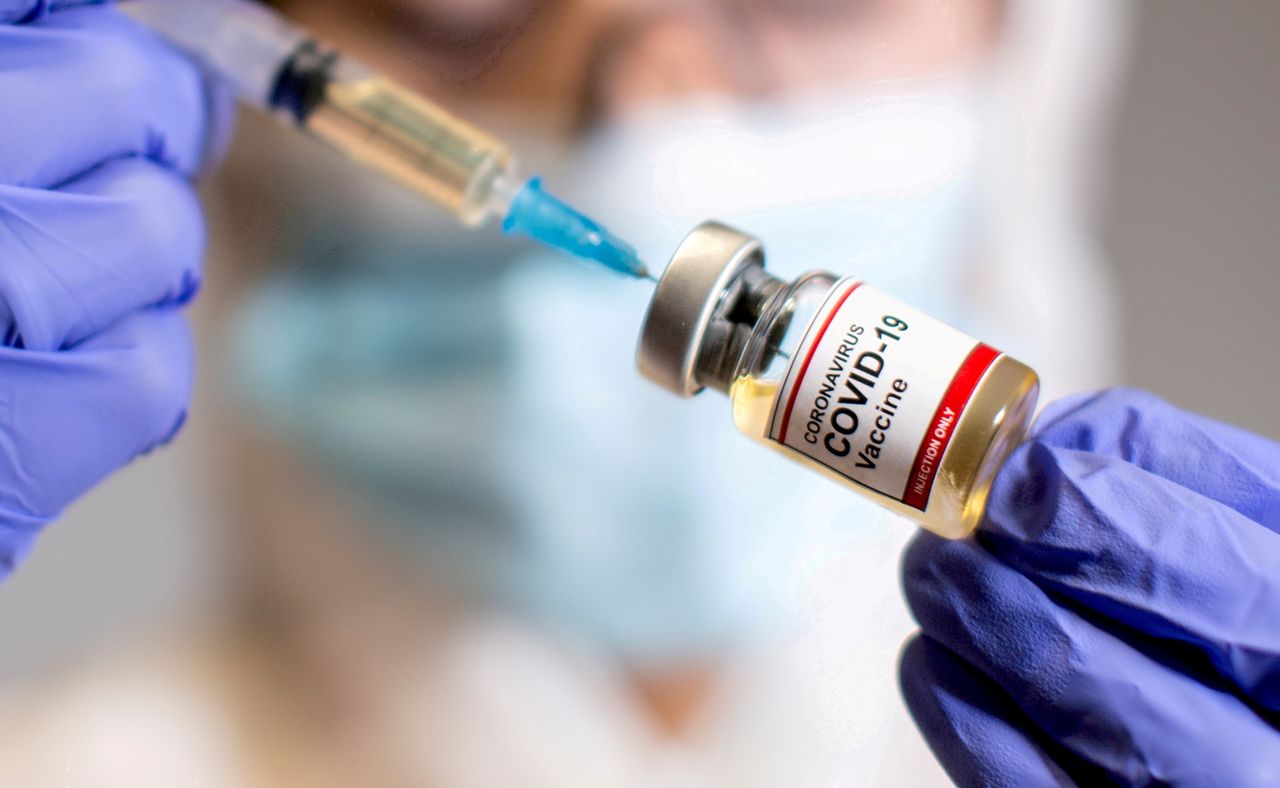 FILE PHOTO: A woman holds a small bottle labelled with a "Coronavirus COVID-19 Vaccine" sticker and a medical syringe in this illustration taken October 30, 2020. REUTERS/Dado Ruvic/File Photo