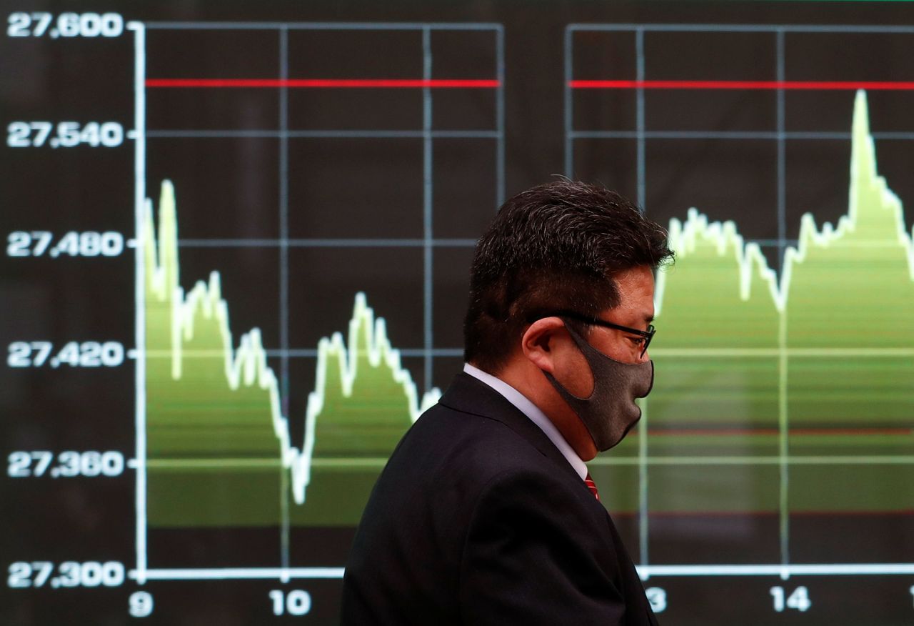 A man wearing a protective face mask walks past a screen displaying a graph showing recent Nikkei share average movements outside a brokerage, amid the coronavirus disease (COVID-19) outbreak, in Tokyo, Japan December 30, 2020. REUTERS/Issei Kato