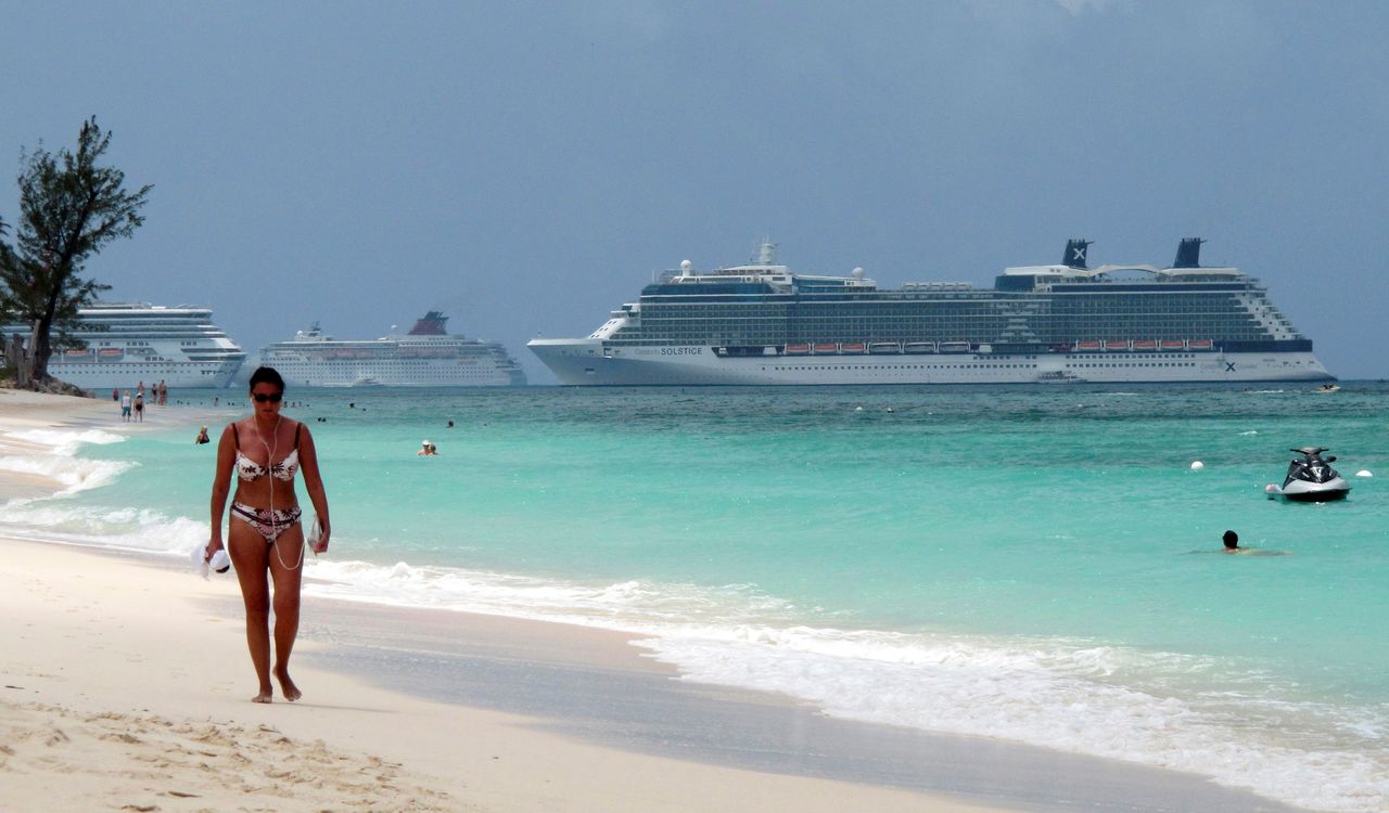 FILE PHOTO: A woman walks along Seven Mile Beach with three cruise ships anchored in port in George Town, Cayman Islands, April 27, 2010. REUTERS/Gary Hershorn/File Photo