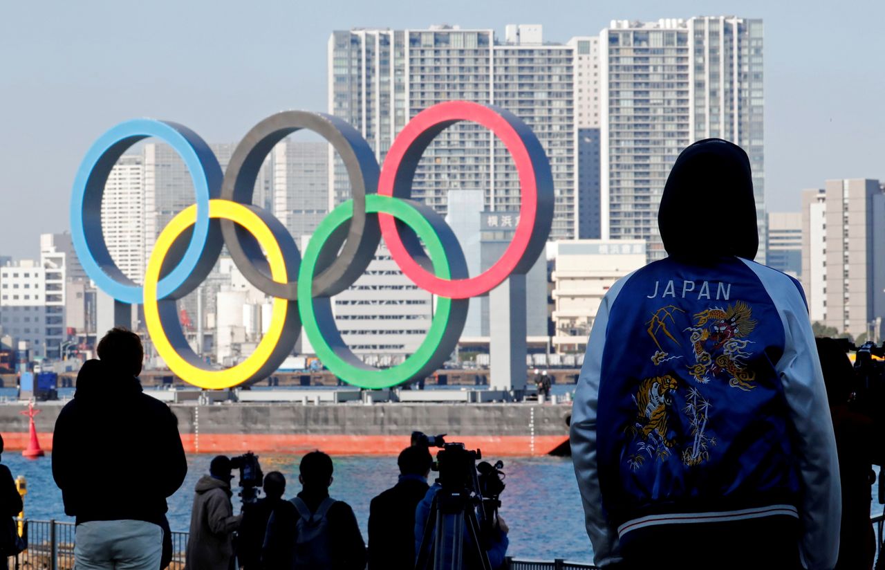 FILE PHOTO: Bystanders watch as giant Olympic rings are reinstalled at the waterfront area at Odaiba Marine Park, after they were temporarily taken down in August for maintenance amid the coronavirus disease (COVID-19) outbreak, in Tokyo, Japan December 1, 2020. REUTERS/Kim Kyung-Hoon/File Picture
