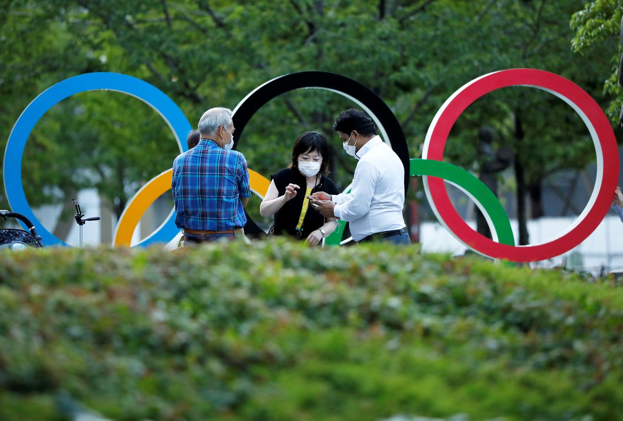 People chat next to Olympic Rings monument outside the Japan Olympic Committee (JOC) headquarters near the National Stadium, the main stadium for the 2020 Tokyo Olympic Games that have been postponed to 2021 due to the COVID-19 pandemic, in Tokyo, June 23, 2021 on the day to mark one month to go until the opening of the Olympic Games. REUTERS/Issei Kato