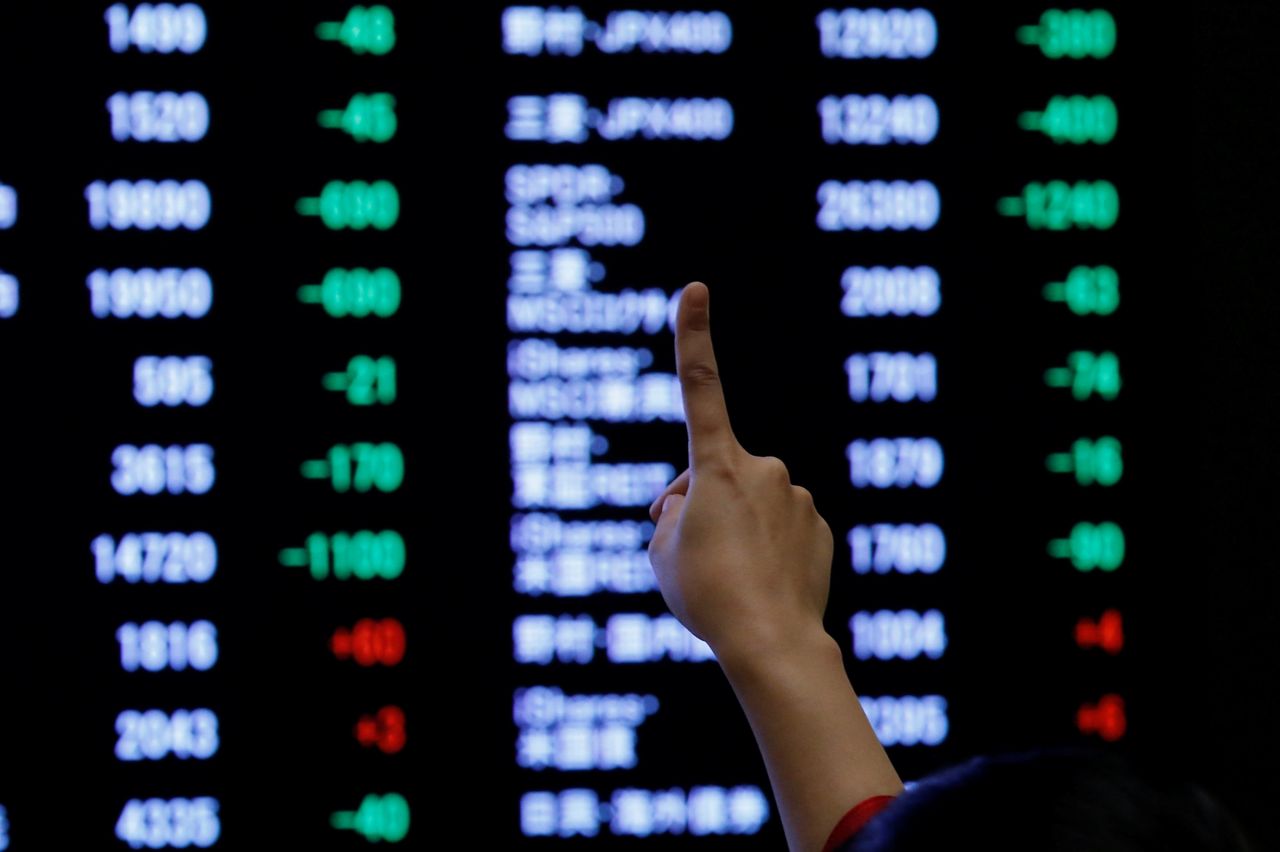 A woman points to an electronic board showing stock prices as she poses in front of the board after the New Year opening ceremony at the Tokyo Stock Exchange (TSE), held to wish for the success of Japan