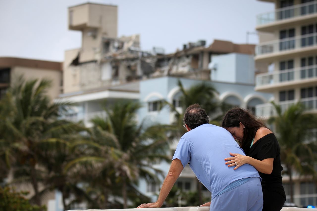 A couple at the beach reacts near the partially collapsed residential building as the emergency crews continue search and rescue operations for survivors, in Surfside, near Miami Beach, Florida, U.S. June 26, 2021. REUTERS/Marco Bello