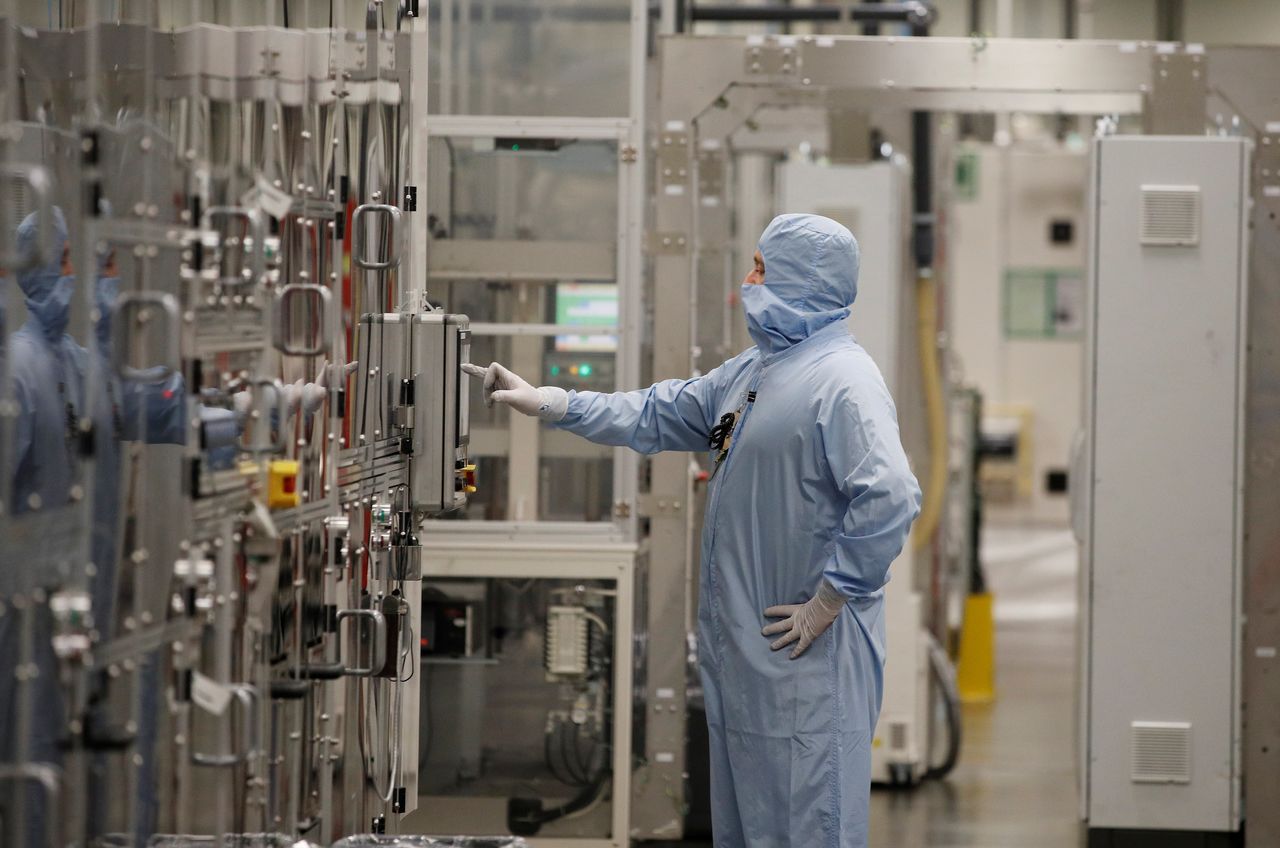 A worker in a protective suit operates a machine inside the Envision battery manufacturing plant at Nissan