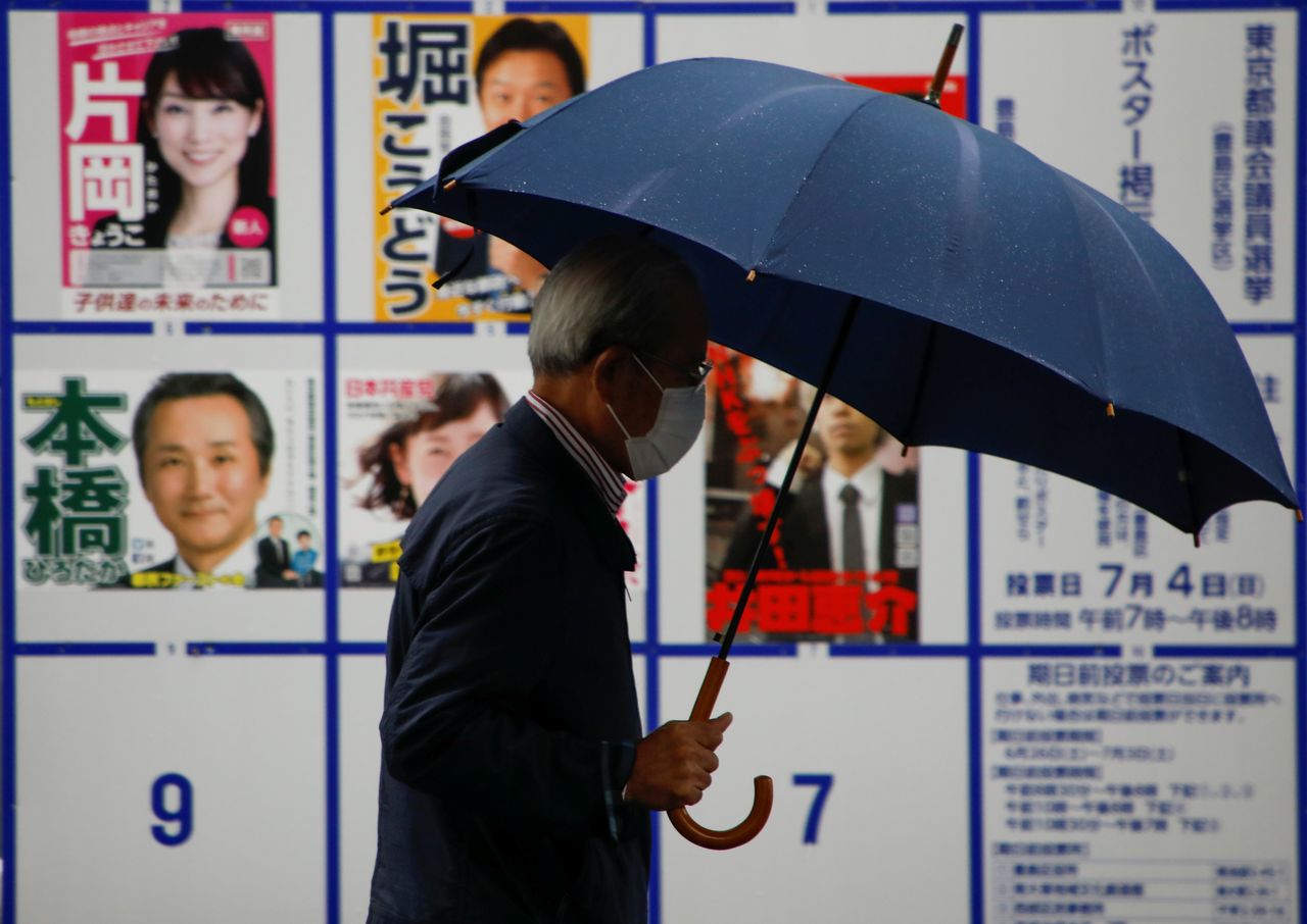 A voter wearing a protective face mask walks past a board displaying posters of candidates for the Tokyo Metropolitan Assembly election near a polling station, amid the coronavirus disease (COVID-19) outbreak, in Tokyo, Japan July 4, 2021. REUTERS/Issei Kato