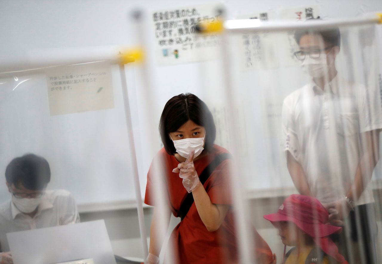 A voter wearing a protective face mask and vinyl gloves is seen between plastic curtains, installed in order to prevent infections following the coronavirus disease (COVID-19) outbreak, at a voting station for the Tokyo Governor election amid the coronavirus disease (COVID-19) outbreak, in Tokyo, Japan July 5, 2020. REUTERS/Issei Kato