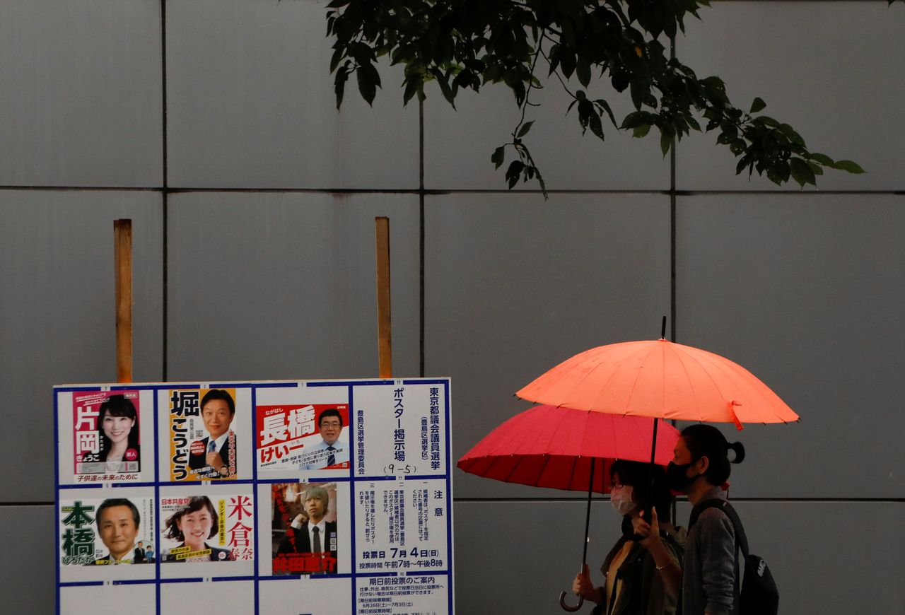 Voters wearing protective face masks walk next to a board displaying posters of candidates for the Tokyo Metropolitan Assembly election near a polling station, amid the coronavirus disease (COVID-19) outbreak, in Tokyo, Japan July 4, 2021. REUTERS/Issei Kato