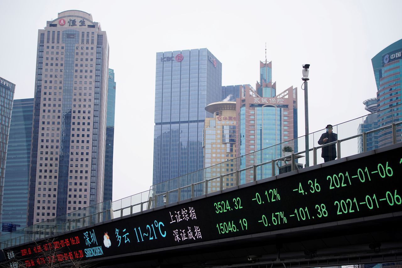 FILE PHOTO: A man stands on an overpass with an electronic board showing Shanghai and Shenzhen stock indexes, at the Lujiazui financial district in Shanghai, China January 6, 2021. REUTERS/Aly Song