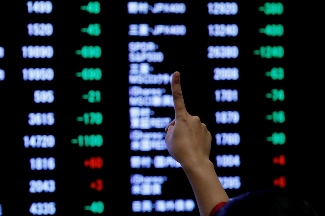FILE PHOTO: A woman points to an electronic board showing stock prices as she poses in front of the board after the New Year opening ceremony at the Tokyo Stock Exchange (TSE), held to wish for the success of Japan