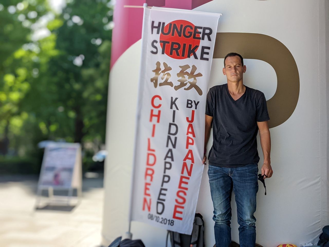 French father-of-two Vincent Fichot stands with his banner where he has been on a hunger strike since July 10 to protest what he says is Japan