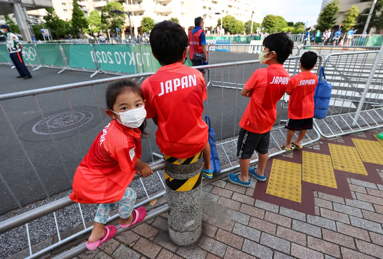 Tokyo 2020 Olympics - Triathlon - Men's Olympic Distance - Final - Odaiba Marine Park, Tokyo, Japan July 26, 2021. Children stand by a barrier as fans and local residents try to catch a glimpse of the men's triathlon event. REUTERS/Issei Kato