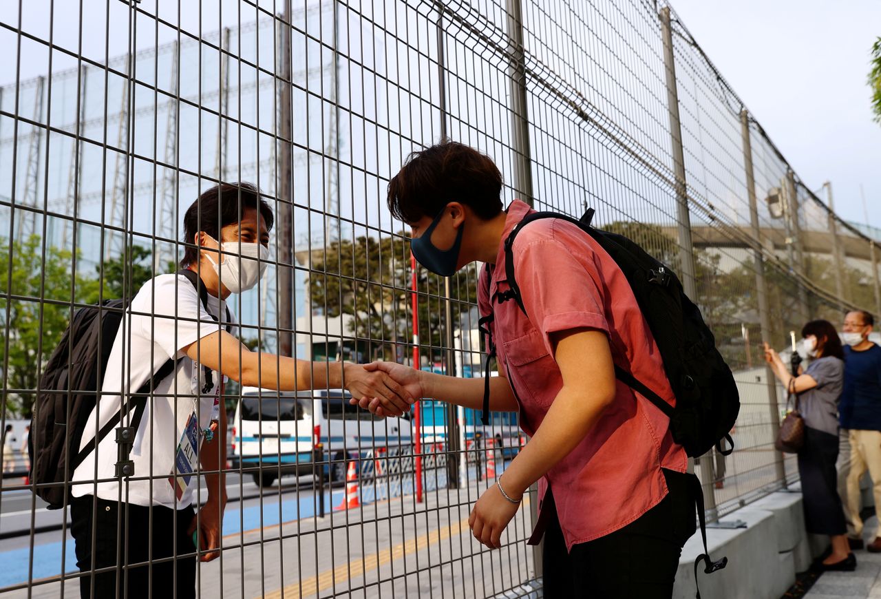 FILE PHOTO: Arisa Tsubata, a nurse and a boxer, shakes hands with a staff member of the opening and closing ceremony of the Tokyo 2020 Olympic Games through a fence outside the National Stadium, the main venue of the Tokyo 2020 Olympic Games in Tokyo, Japan, July 26, 2021. Picture taken on July 26, 2021. REUTERS/Kim Kyung-Hoon/File Photo