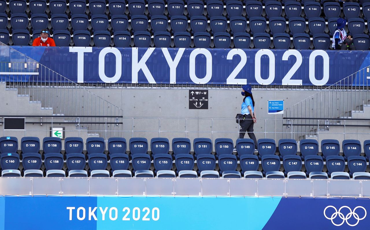 FILE PHOTO: A spectator sits as a volunteer walks beaneath a logo during the Tokyo 2020 Olympic Games in at the Oi Hockey Stadium in Tokyo, Japan, July 24, 2021. REUTERS/Siphiwe Sibeko