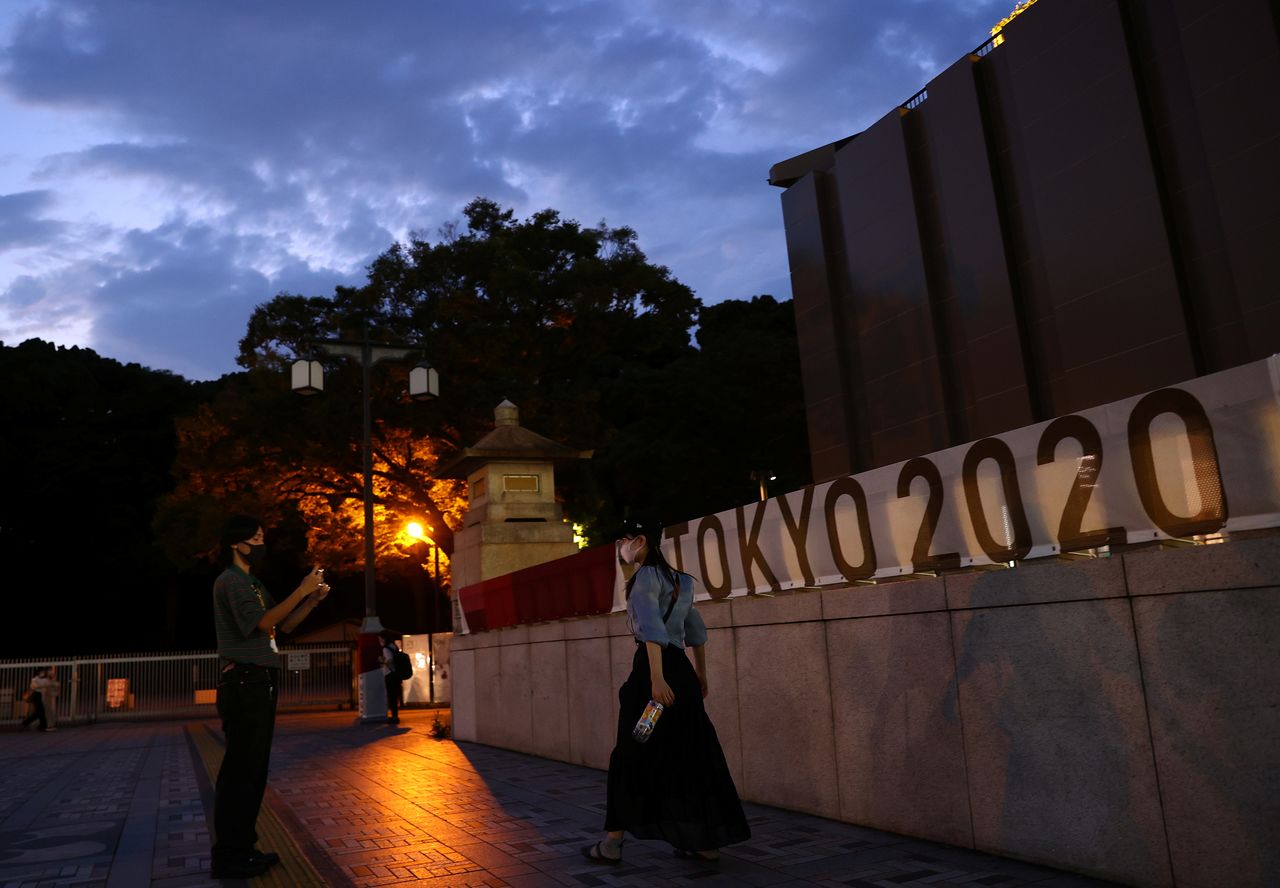 A couple wearing protective masks, amid the coronavirus disease (COVID-19) outbreak, takes a photo in front of a banner of Tokyo 2020 Olympic Games in Tokyo, Japan, July 28, 2021. REUTERS/Kim Kyung-Hoon