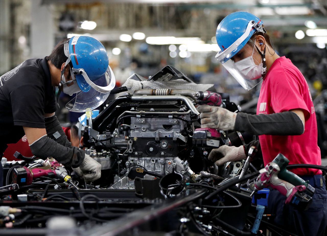 Employees wearing protective face masks and face guards work on the automobile assembly line, during the outbreak of the coronavirus disease (COVID-19), at Kawasaki factory of Mitsubishi Fuso Truck and Bus Corp., owned by Germany-based Daimler AG, in Kawasaki, south of Tokyo, Japan May 18, 2020. REUTERS/Issei Kato