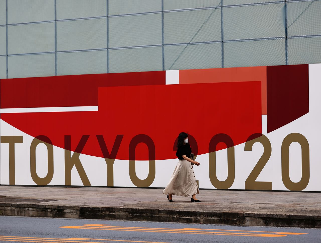 FILE PHOTO: A woman, wearing a protective mask against COVID-19, walks past a wall bearing logo of Tokyo 2020 Olympic Games in Tokyo, Japan, July 29, 2021. REUTERS/Kim Kyung-Hoon
