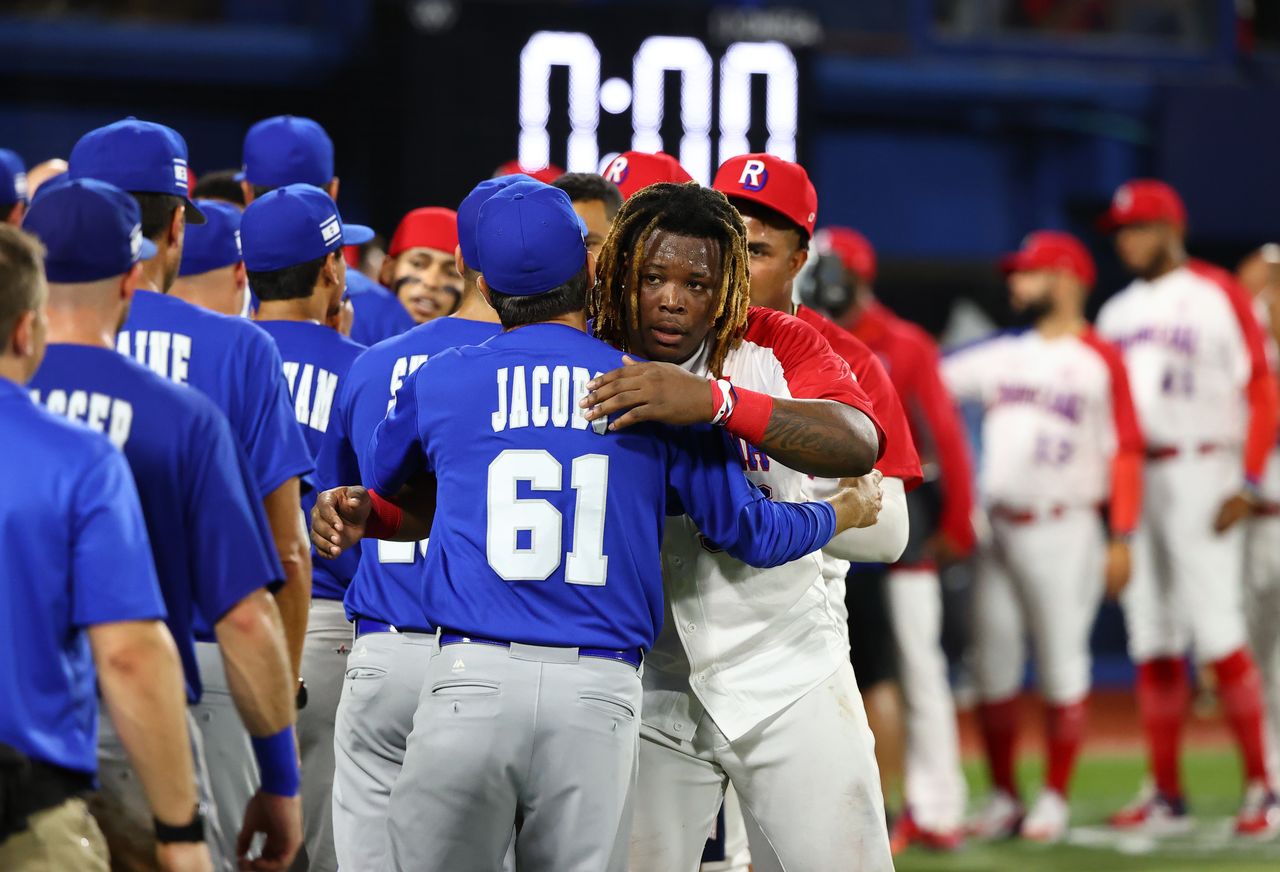 Tokyo 2020 Olympics - Baseball - Men - Round 1 Repechage - Israel v Dominican Republic - Yokohama Baseball Stadium, Yokohama, Japan - August 3, 2021. Johan Mieses of the Dominican Republic hugs Israel coach Alex Jacobs as players congratulate each other after the game. REUTERS/Jorge Silva