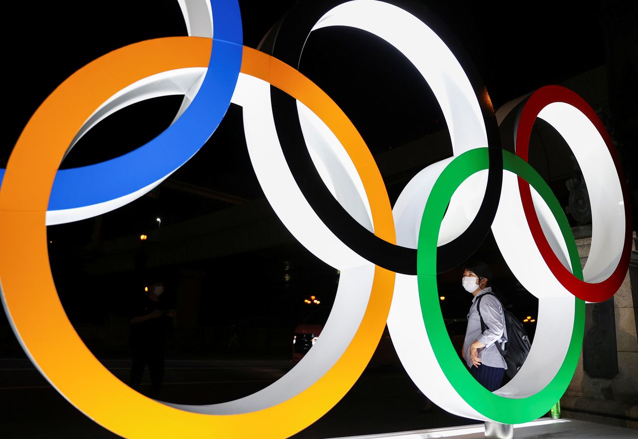 A woman wearing a protective face mask is seen through an illuminated Olympic Rings monument during the Tokyo 2020 Olympic Games, amid the coronavirus disease (COVID-19) pandemic, in Tokyo, Japan, August 5, 2021. REUTERS/Issei Kato