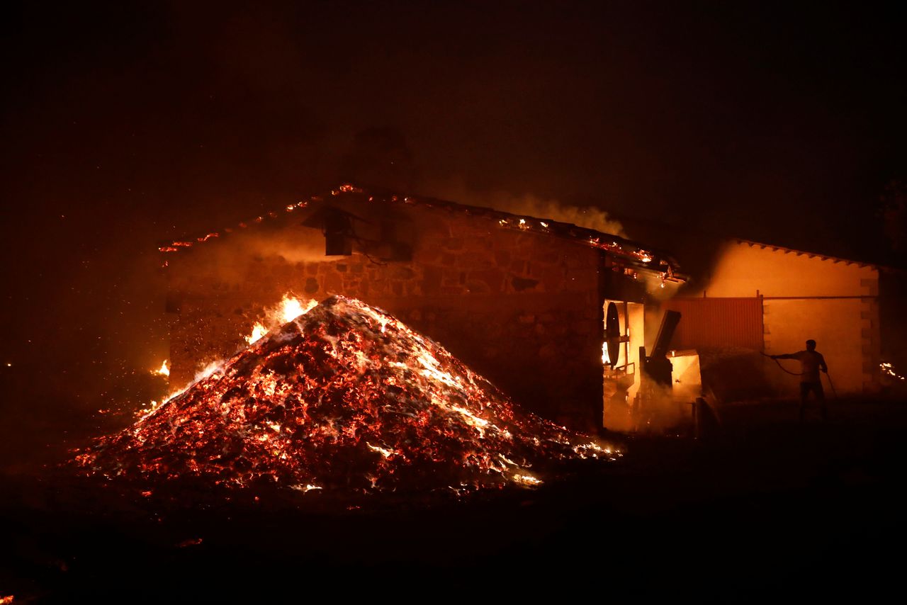 A man sprays water on a burning olive press factory during a wildfire in the village of Rovies, on Evia island, Greece, August 4, 2021. REUTERS/Costas Baltas