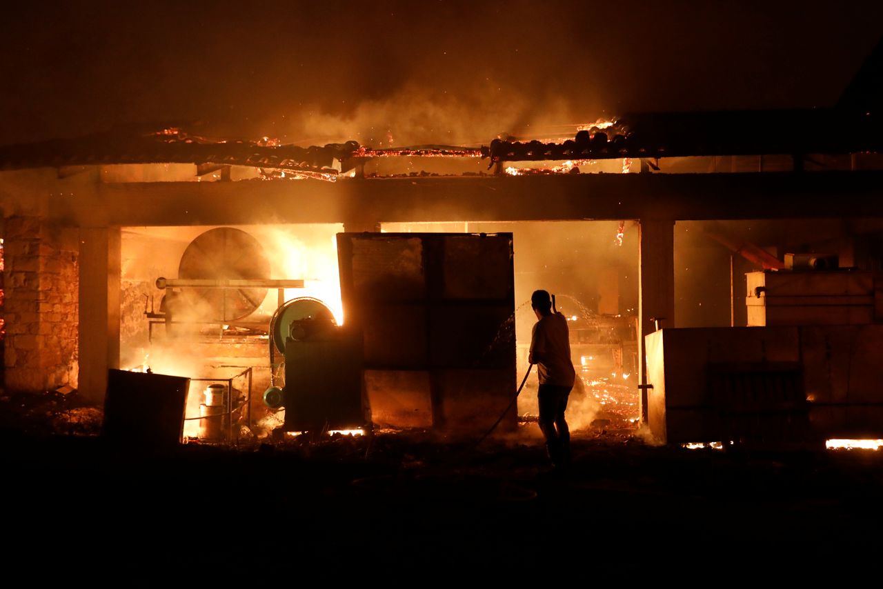 A man sprays water on a burning olive press factory during a wildfire in the village of Rovies, on Evia island, Greece, August 4, 2021. REUTERS/Costas Baltas