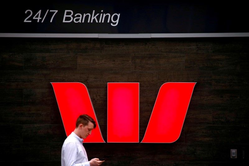 FILE PHOTO: FILE PHOTO: A pedestrian looks at his phone as he walks past a logo for Australia