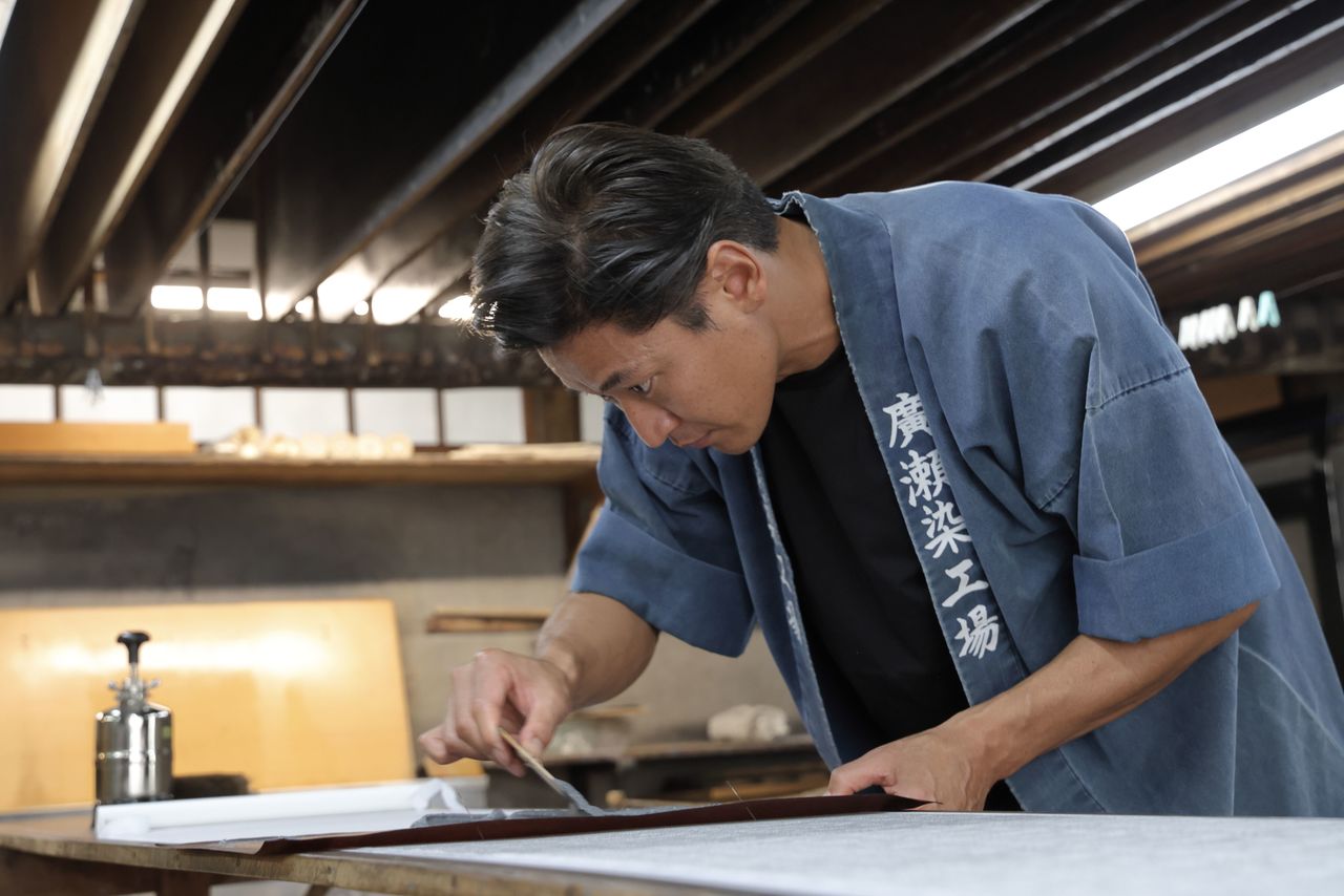 A mixture of glue and dye is applied to the fabric through the stencil. The number of people present in the workshop can affect humidity, so the pace of the work needs to be adjusted accordingly. (© Hanai Tomoko)