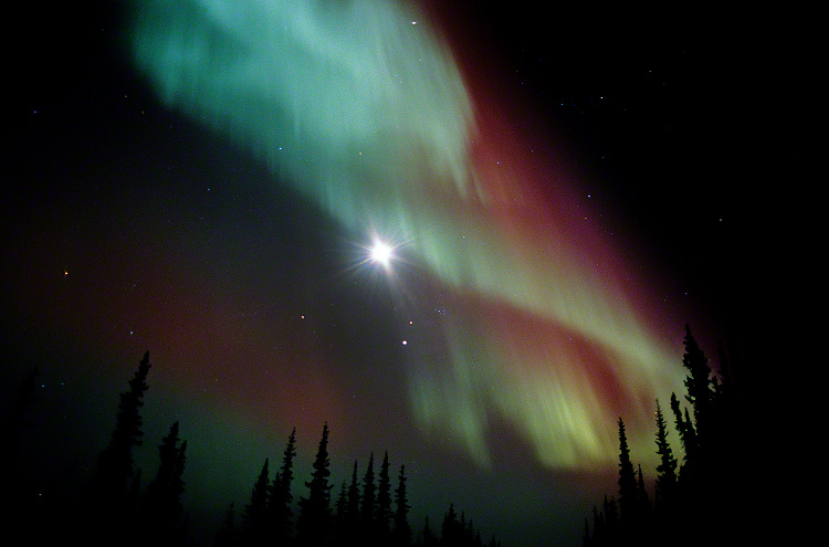 The Aurora Borealis dances across the face of the full moon.