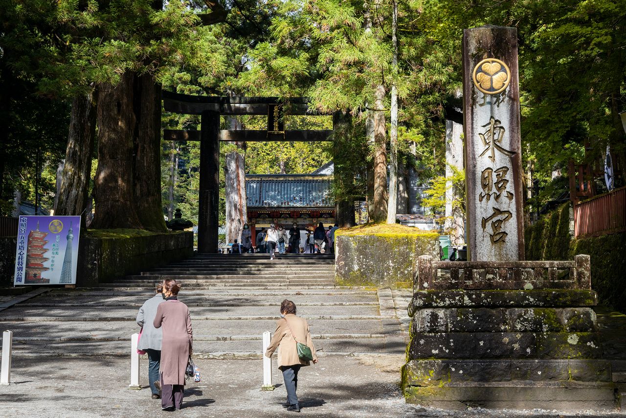 El emblema dorado de los Tokugawa, compuesto por tres hojas de malvarrosa, destaca sobre la piedra del monumento situado delante de las escaleras que conducen al santuario. (Imagen de la redacción de nippon.com)