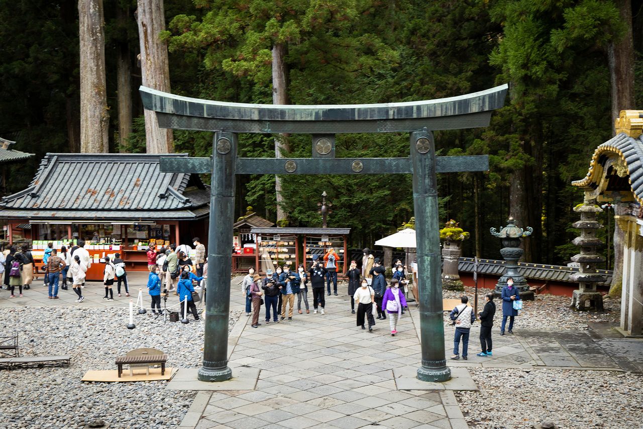 El torii de bronce visto desde la puerta Yōmei. En esta imagen se aprecia a un grupo de personas cámara en mano. (Imagen de la redacción de nippon.com)