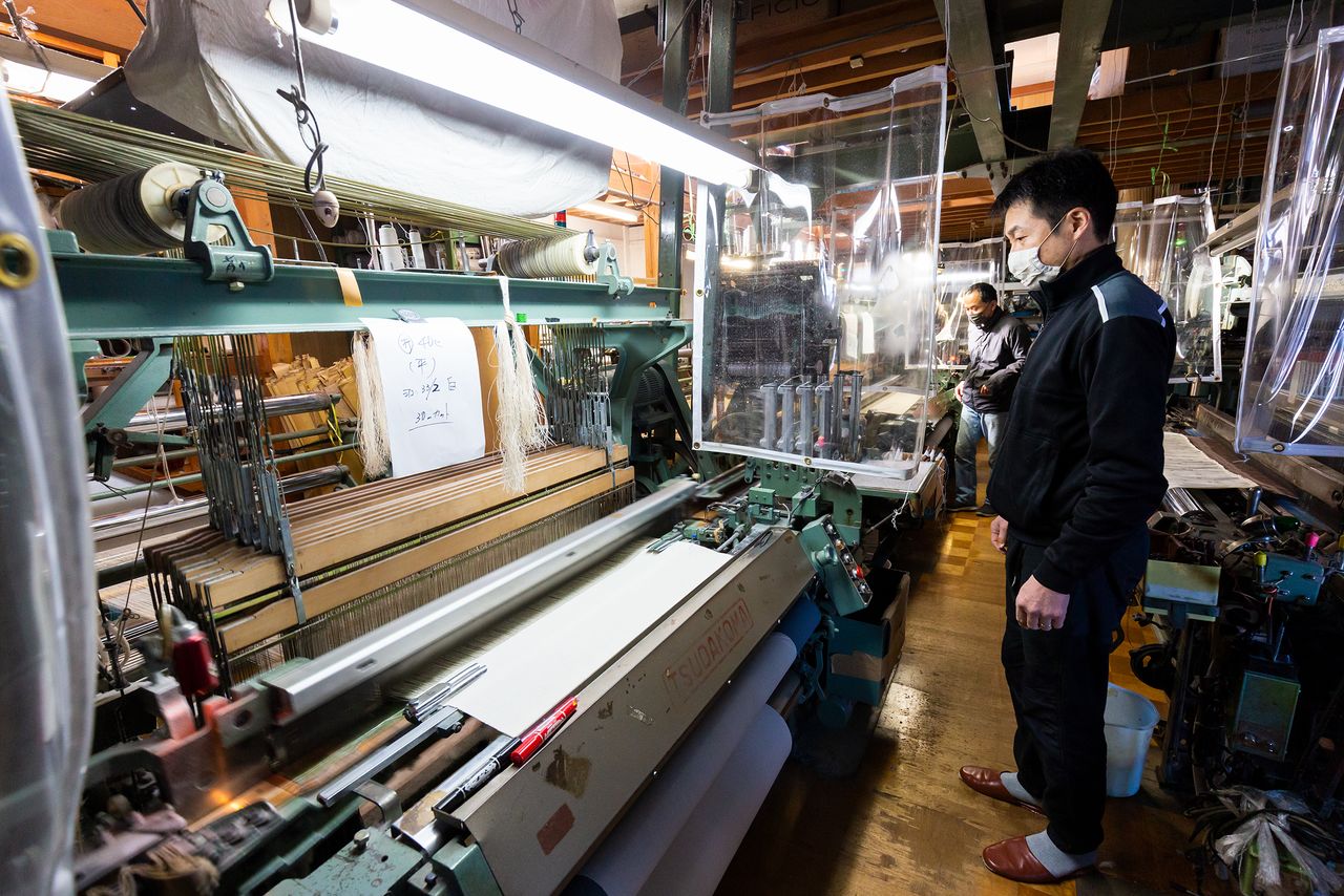 Kobayashi examinando el funcionamiento de una máquina de tejer. Dependiendo de la tela, es preferible usar máquinas antiguas para su producción.