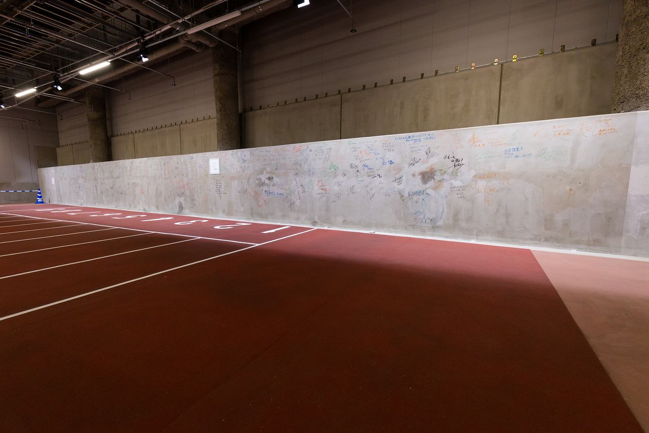 Cerca del estacionamiento de los autobuses que trasladaban a los deportistas está la pared de hormigón que los deportistas autografiaron después de las competiciones.