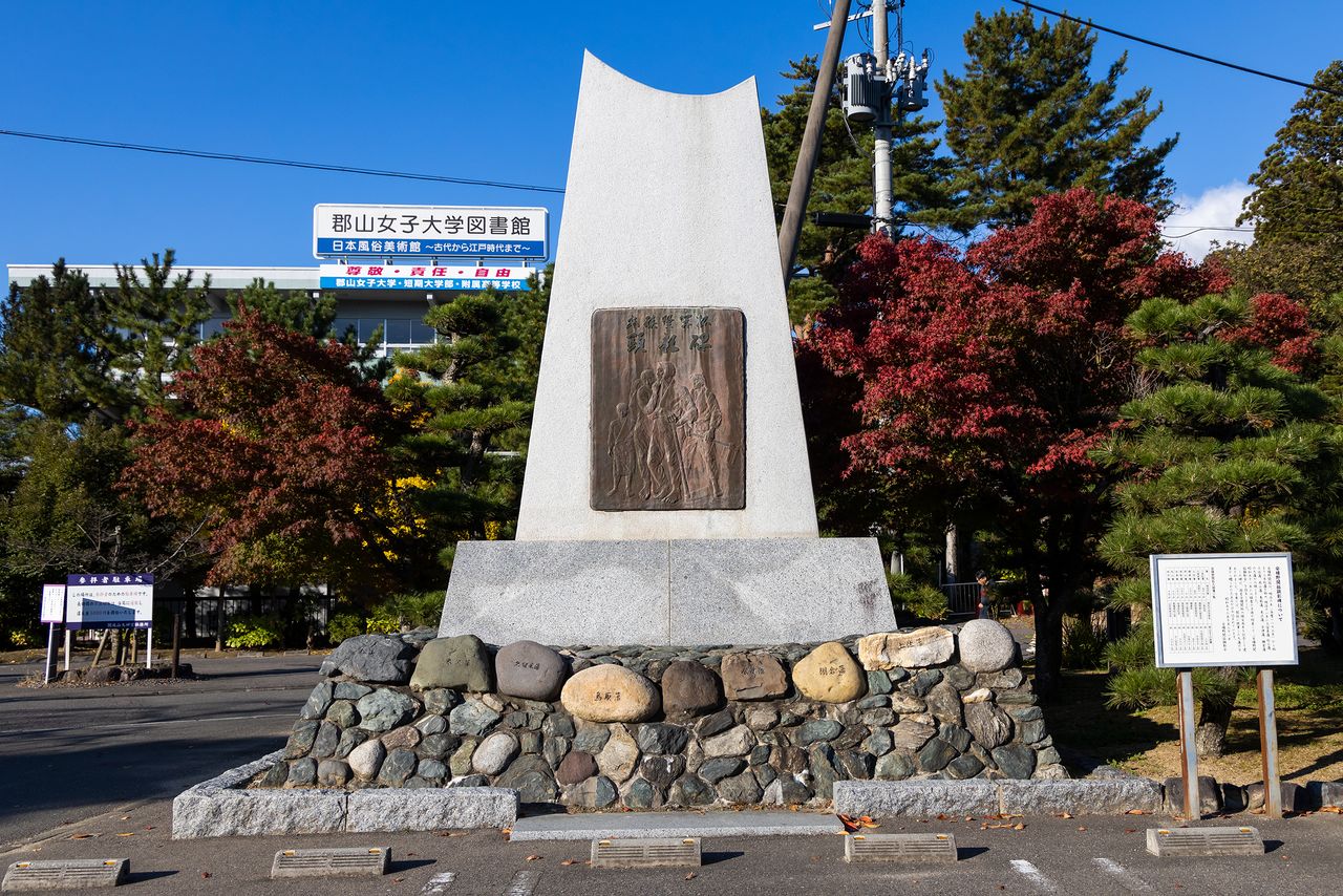 La piedra del pedestal del Monumento Conmemorativo de los Pioneros de Asaka tiene grabados, desde la izquierda, los nombres de los dominios de Matsuyama, Yonezawa, Kurume, Tottori, Nihonmatsu, Aizu, Tanagura, Tosa y Okayama.
