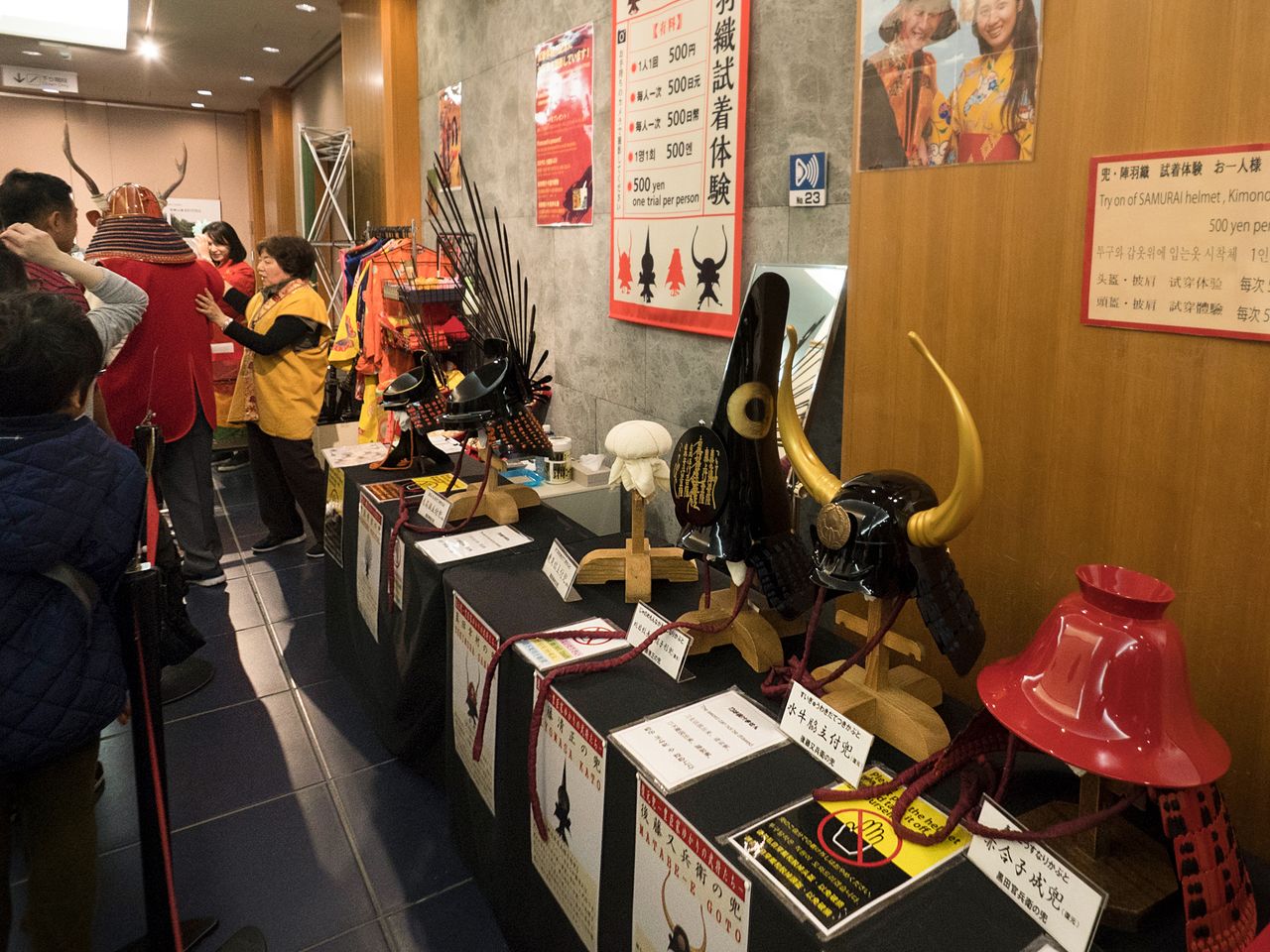 Hay una gran variedad de cascos disponibles para probarse. De derecha a izquierda, el casco del señor feudal Kuroda Kanbei, el del samurái Gotō Matabei, el de Katō Kiyomasa y el de Hideyoshi. Al fondo, un hombre probándose el de Sanada Yukimura. 