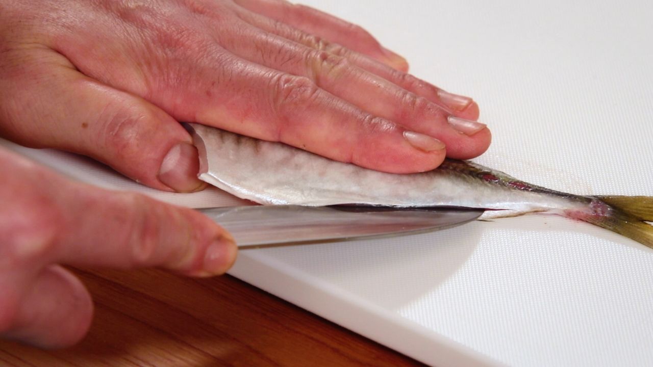 Gire el pescado 180 grados, inserte el cuchillo a lo largo de la tripa y corte hasta que llegue a la espina.