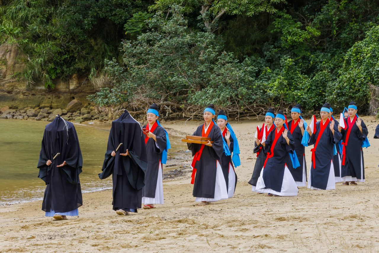 La procesión de hudamichi (con la cabeza cubierta con un manto negro) y angā avanza por la playa siguiendo al dios Miriku.