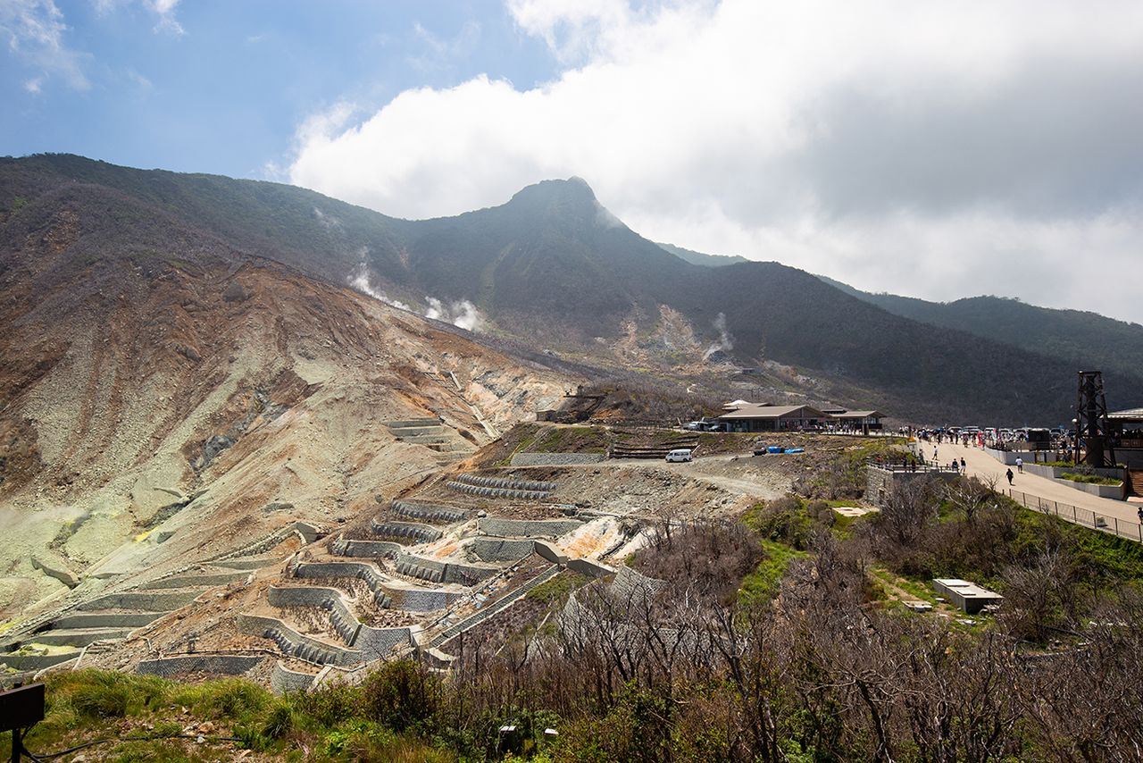 La cima en el centro es el monte Kanmurigatake (1.409 metros sobre el nivel del mar) y la zona de fumarolas se extiende por debajo. El valle de la izquierda es Ōwakusawa, que ha sufrido repetidos deslizamientos de tierra a gran escala y está siendo sometido a trabajos de control de la erosión.