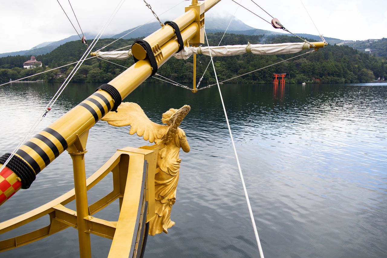 El Queen Ashinoko cruza las aguas del lago Ashinogo guiado por la diosa de la victoria. El santuario de Hakone y el Torii de la Paz se pueden ver en la dirección de la marcha.
