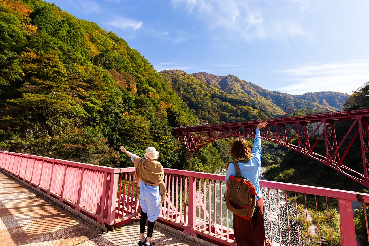 Dos mujeres en el puente de Yamabiko saludan al tren que pasa por el puente de Shin-Yamabiko.