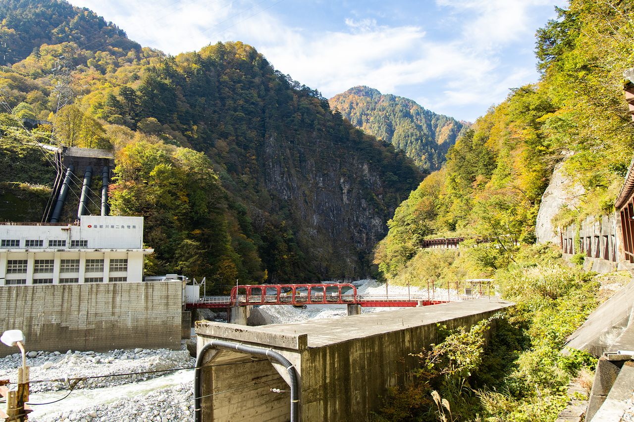 Detrás del puente rojo metálico que corresponde a la segunda planta de generación eléctrica de Kurobe se aprecia el peñasco Nezumi-gaeshi, que tiene una altura de 200 metros.