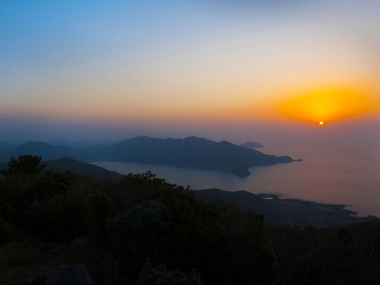 La vista de Yagatame, isla de Nakadōri, desde la costa contraria. El sol del atardecer colorea el mar y el cielo. 